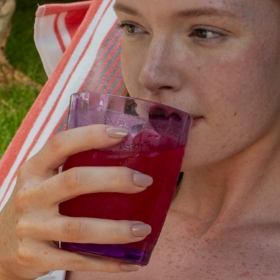 Woman laying out by the pool and sipping a drink with Youth Factor Antioxidant Boost Powder